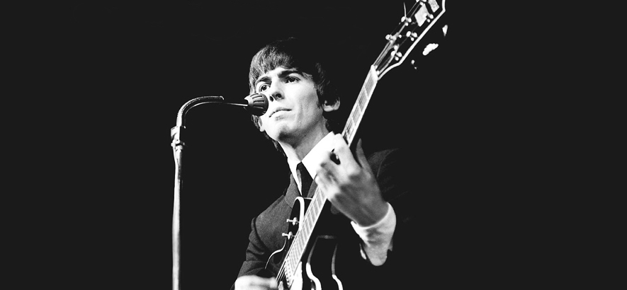 Schwarz-weiß Aufnahme des Beatles George Harrison mit Gitarre am Mikrofon.
