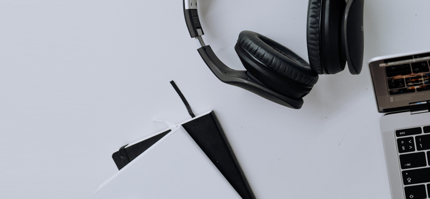 Foto eines Kopfhörers, eines Notizhefts und eines Laptops auf einem Tisch liegend