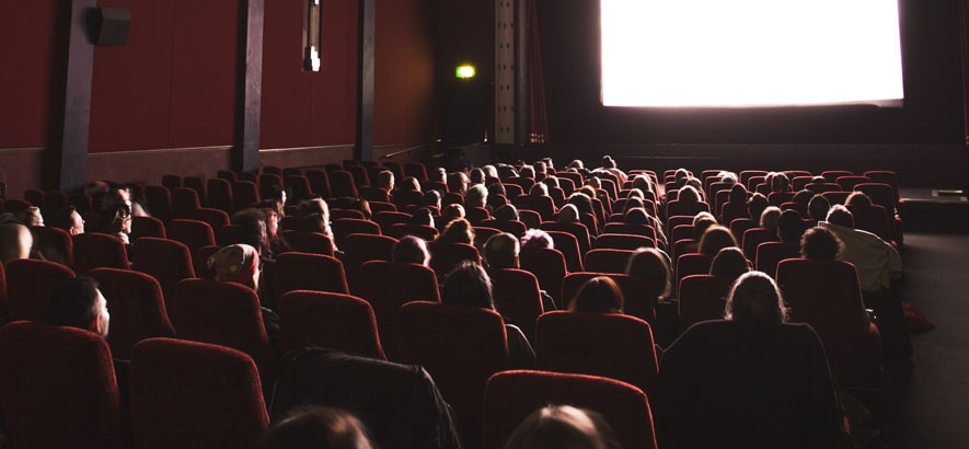 Foto eines Kinosaals mit Besucher*innen, die auf die erleuchtete Leinwand schauen