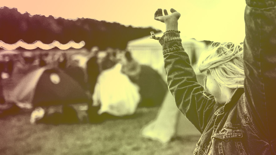 Foto einer Frau auf einem Festivalgelände, die die Arme in die Luft wirft