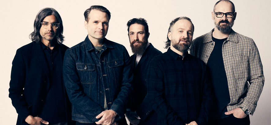 Pressefoto von Death Cab For Cutie, die im Musikvideo zu ihrer neuen Single „Here To Forever“ im Presswerk aushelfen.