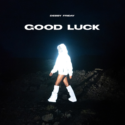 Cover des Albums „Good Luck“ von Debby Friday, das die Musikerin in einer weißen, leuchtenden Daunenjacke in einer düsteren Umgebung zeigt.