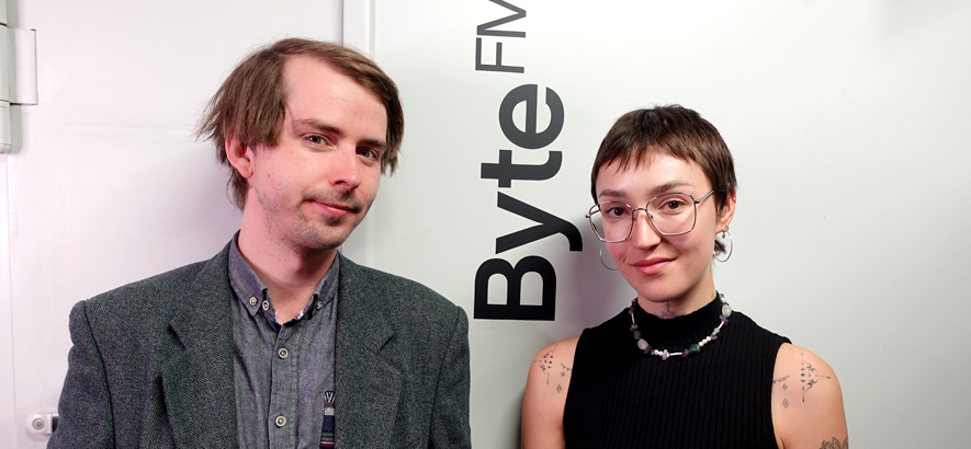 Foto der ByteFM Moderator*innen Marius Magaard und Lena Boßmann vor einer weißen Tür mit ByteFM-Logo