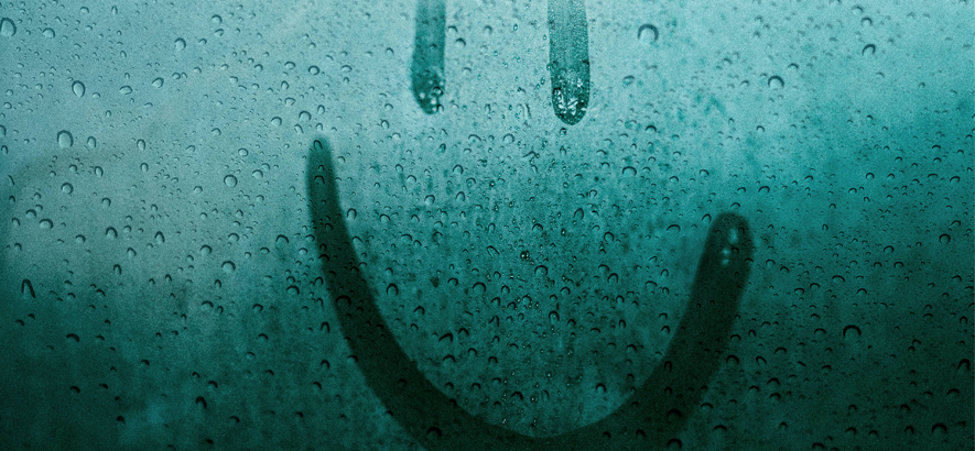 Foto einer mit Regentropfen benetzten Fensterscheibe, auf die ein Smiley-Gesicht gemalt ist